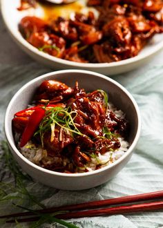 two bowls filled with meat and rice next to chopsticks on a tablecloth