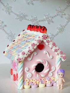 a pink birdhouse with cupcakes and candy on the roof is next to a small doll