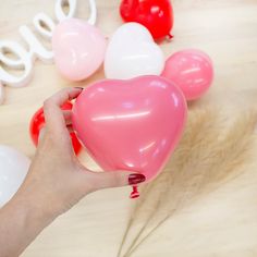 a person holding a heart shaped balloon in front of some balloons on a table with the word love spelled out