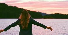 a woman with her arms outstretched standing in front of the water at sunset or sunrise