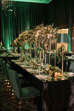 a long table is set up with green velvet chairs and tall centerpieces on it