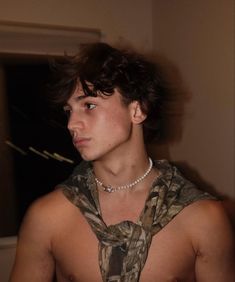 a young man wearing a pearl necklace and camouflage shirt looking off into the distance with his hand on his hip