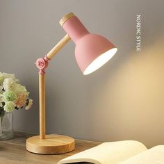 a pink lamp sitting on top of a wooden table next to a vase with flowers