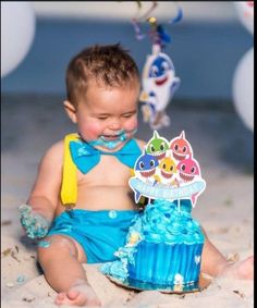 a baby sitting in the sand with a blue cake and decorations on it's face