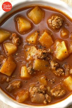 a white bowl filled with stew and potatoes on top of a wooden table next to a spoon