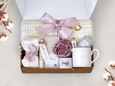 an open box with some items in it and a pink ribbon around the top, on a white surface