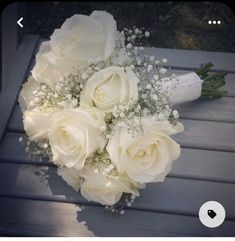 a bridal bouquet with white roses and baby's breath is sitting on a bench