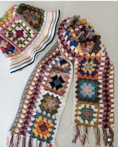 two crocheted scarves are sitting on a table together, one is multicolored and the other has fringes