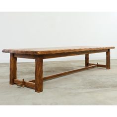 a large wooden bench sitting on top of a cement floor next to a white wall