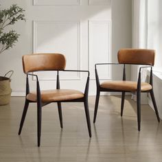 two brown chairs sitting next to each other on top of a hard wood floor in front of a white wall