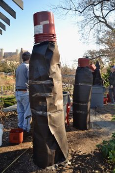 two men standing next to each other in front of trees and bushes with plastic bags wrapped around them