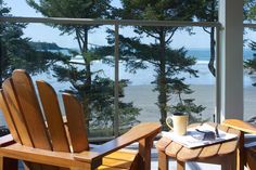 two wooden chairs sitting next to each other on top of a porch near the ocean