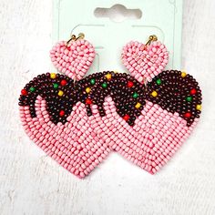 pink and black beaded heart shaped earrings on white table next to small card board