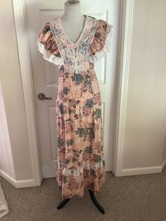 This nice vintage 70s peach burgundy green floral lace bib high waisted Maxi hippie dress comes to you in a size S. As you can see from pictures lace bodice over and then ties in back. Looks to be handmade cannot find a tag. Up material etc points to 70s dress.pls compare the measurements I give you to those in your closet. Overall great cond. 17 1/4 underarm to underarm -14/inches waist across- hips n/a-46 1/4 inches underarm to bottom of dress. Bohemian Floral Print Dress With Empire Waist, Bohemian Fitted Maxi Dress With Lace Patchwork, Fitted Bohemian Maxi Dress With Lace Patchwork, Bohemian Pink Lace Dress, Vintage V-neck Dress For Garden Party, Bohemian Summer Dress With Lace Bodice, Cottagecore V-neck Dress With Lace Trim, Fitted Festival Maxi Dress With Lace Trim, Summer Dress With Empire Waist And Lace Bodice