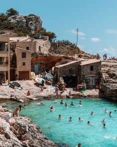 many people are swimming in the water near some buildings and cliffs, while others swim in the ocean