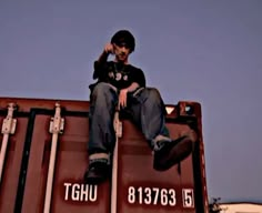 a man sitting on top of a dumpster talking on a cell phone