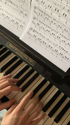 two hands playing the piano with sheet music behind them