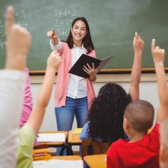 a teacher teaching in front of her class with students raising their hands and pointing to the chalkboard