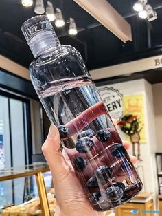 a person holding up a water bottle with blueberries in it