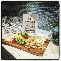 a wooden cutting board topped with grapes and cheese next to wine glasses on a counter