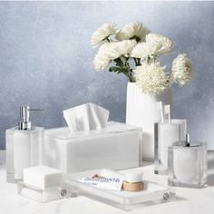 white bathroom accessories including soap, toothbrushes and flowers in a vase on a table