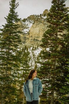 a woman standing in the snow near some trees and mountains with a mountain behind her