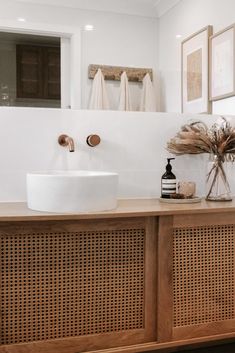 a white sink sitting on top of a wooden counter next to a mirror and framed pictures