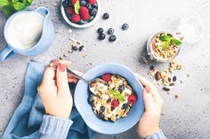 a person eating granola with berries, yogurt and blueberries on the side