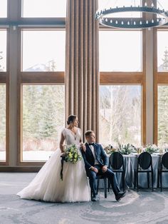 a bride and groom sitting in front of large windows