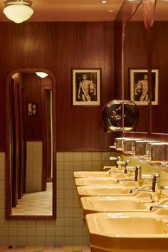 a row of sinks in a bathroom with pictures on the wall