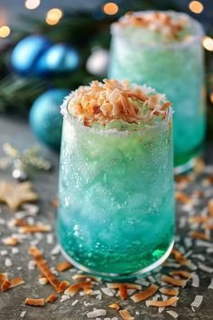 two glasses filled with blue and green drinks on top of a table next to christmas decorations