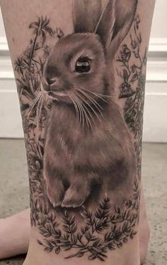 a black and white tattoo of a rabbit on the leg, with flowers around it