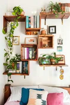 a bed topped with lots of books next to a wall mounted shelf filled with plants