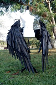 a white mannequin with black wings sitting in the grass