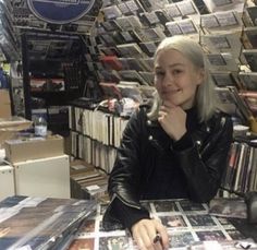 a woman sitting at a table in front of a record store filled with records and cds