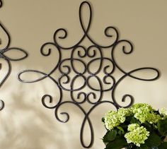 two wrought iron wall hangings with green flowers in the foreground and a vase on the right