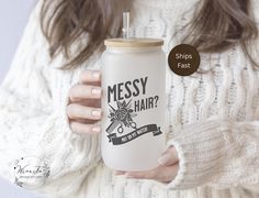 a woman holding a white coffee mug with the words messy hair on it