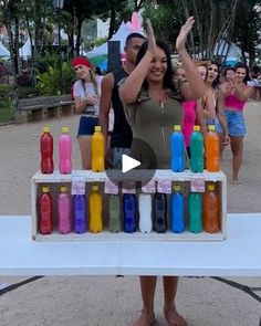 a woman standing in front of a table with bottles on it and people behind her