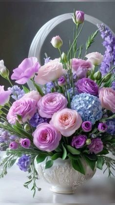 a white vase filled with lots of purple and blue flowers on top of a table