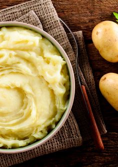 a bowl filled with mashed potatoes on top of a cloth next to two whole potatoes