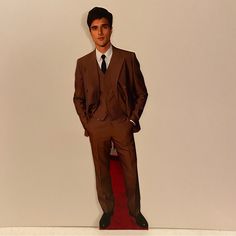 a man in a brown suit and tie standing on a red carpet with his hands in his pockets