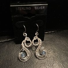 silver earrings sitting on top of a black leather table next to a card and box