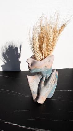 a vase with wheat in it sitting on a table next to a shadow of a person