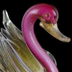 a pink and gold glass swan figurine on a black background