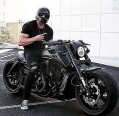 a man sitting on a motorcycle in a parking lot with his hand on the seat