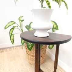 a white vase sitting on top of a wooden table next to a potted plant