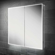 an illuminated bathroom mirror in the corner of a tiled wall next to a white sink