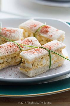 small sandwiches on a white plate with green garnish