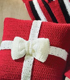 two red crocheted pillows with a white bow on one pillow and a black and white knitted pillow