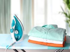 an ironing board with clothes on it and a potted plant in the background